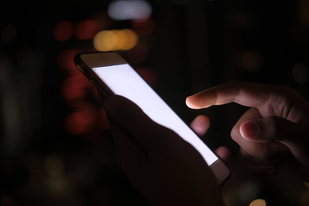 Tangan memegang ponsel cerdas di malam hari dengan cahaya kota